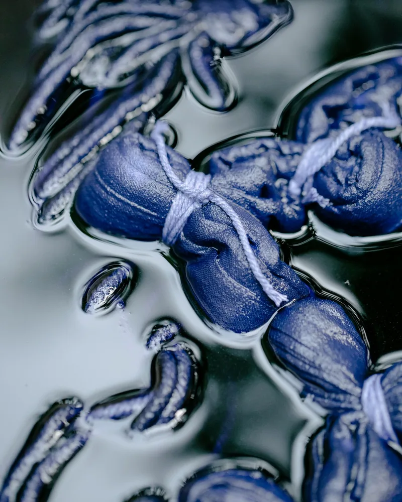Piezas de tela atadas con hilo sumergidas en un baño de índigo, con el tejido teñido de azul profundo bajo la superficie del líquido
